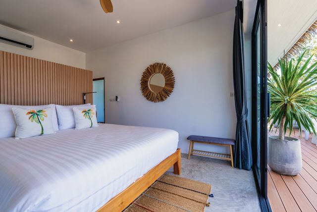 Bedroom with a slatted timber headboard and white linen opening to the pool deck at a Pahili villa