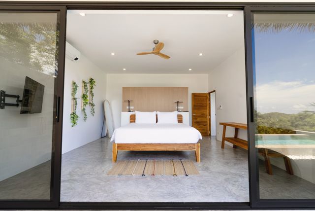 Bedroom with sliding glass doors framing the hills and pool at a Pahili villa