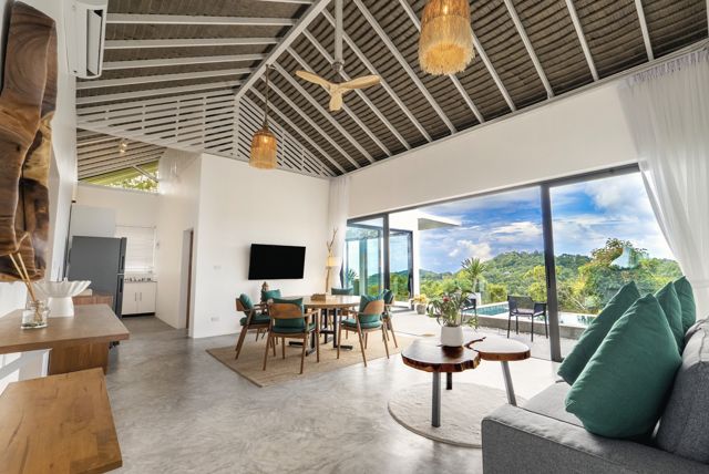 Open-plan living and dining room with a slatted timber ceiling and floor-to-ceiling views at a Pahili villa