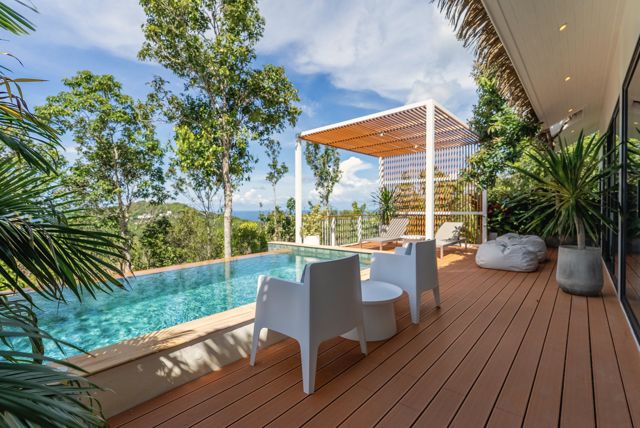 Infinity pool and timber deck with white lounge chairs looking over the jungle at a Pahili villa